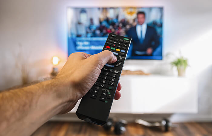 hand with remote control for tv in background