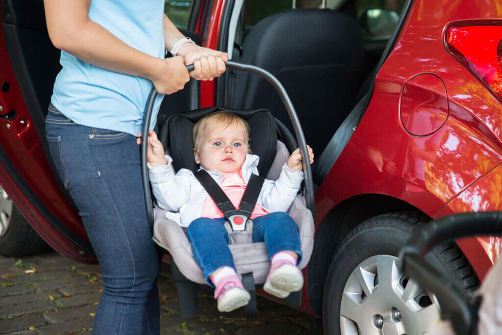 Person holding baby carrier with baby in front of a car with the door open