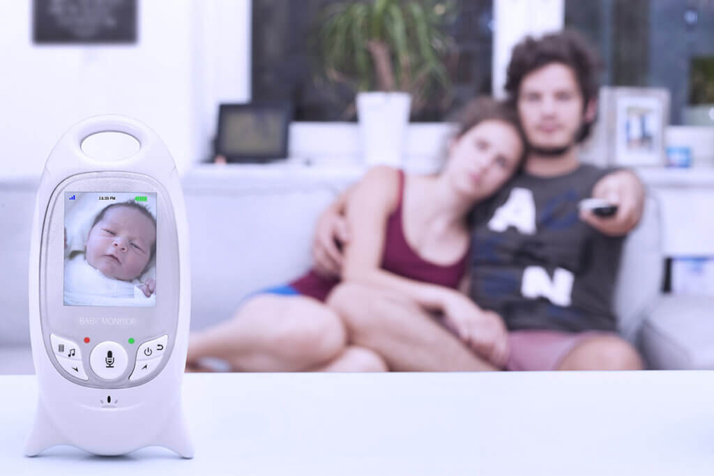 Young couple sitting on sofa with baby monitor in front
