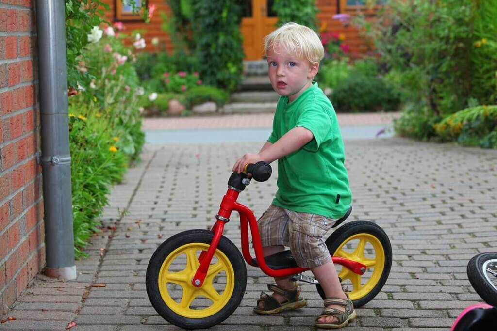 small boy rides on balance bike through park