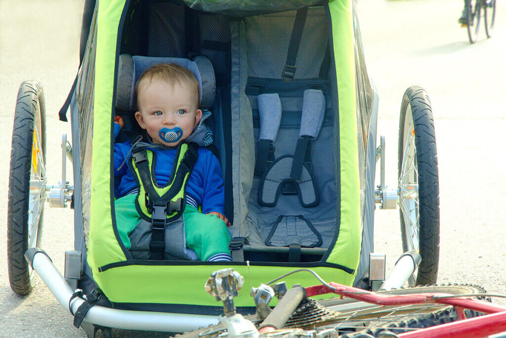 Toddler sitting in green bicycle trailer