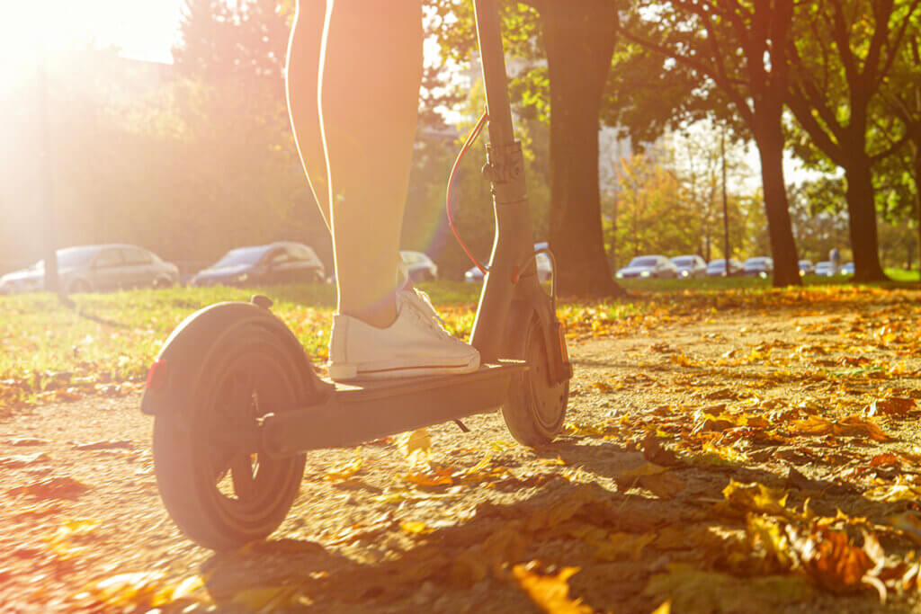 person rides with scooter through autumn leaves