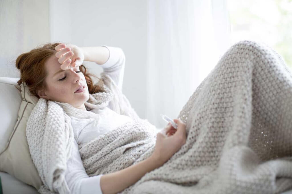 woman lying with fever in bed and loking up thermometer