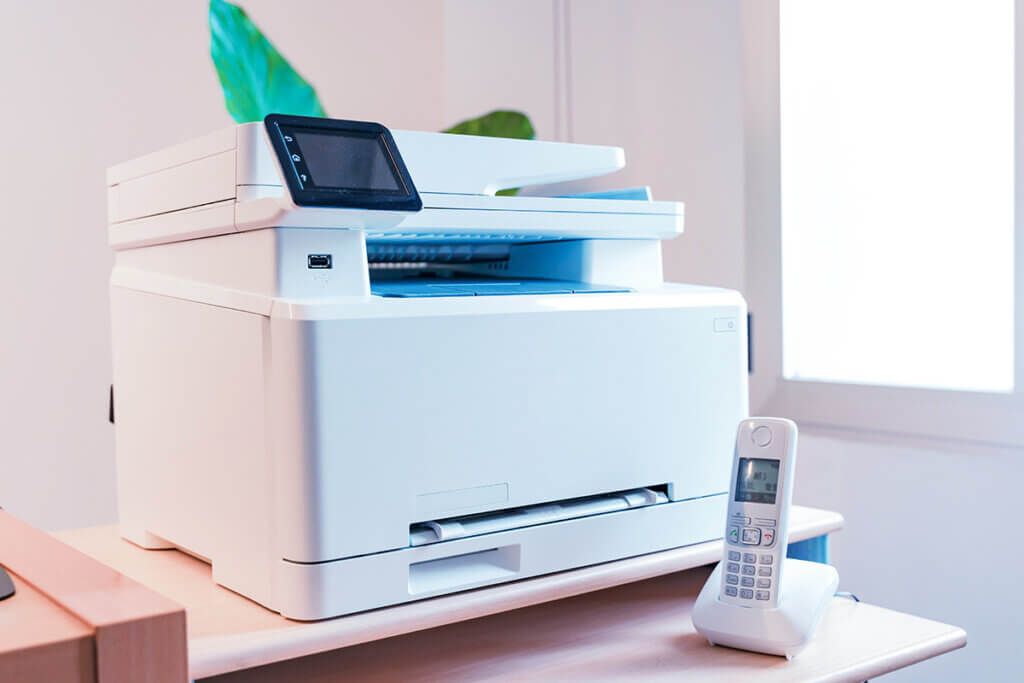  A white multifunction printer stands in a bright office.