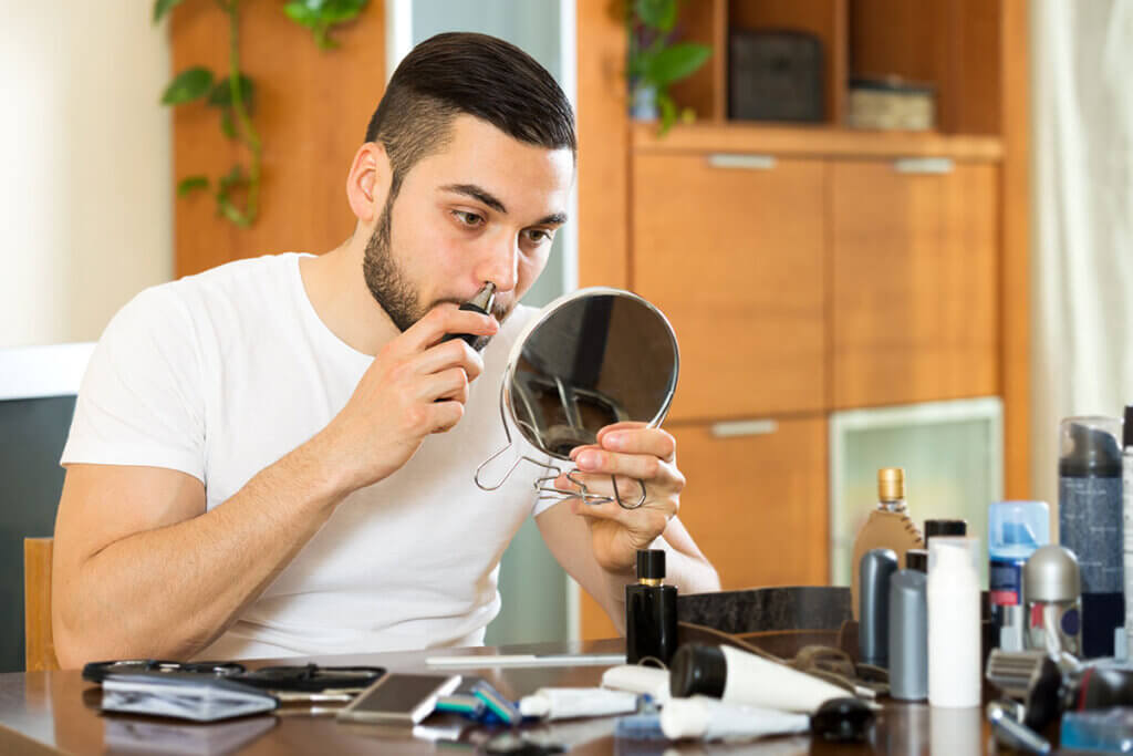 Man trimming nose hair in front of small mirror
