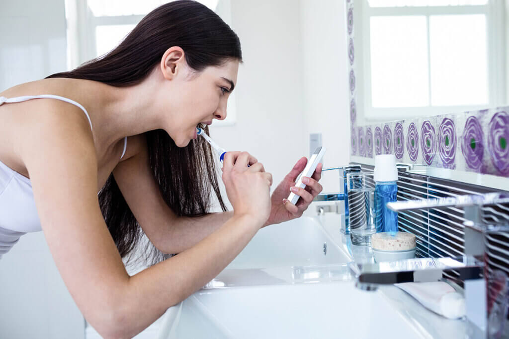 woman ueses smartphone when brushing