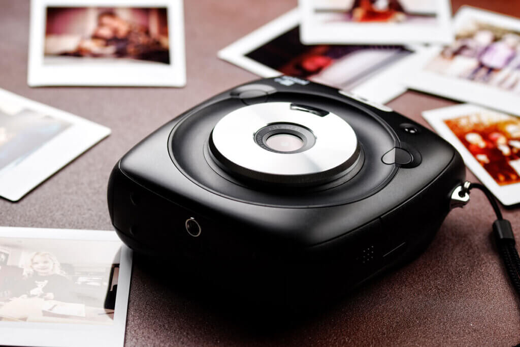 A modern instant camera lies on a table with the photos next to it.