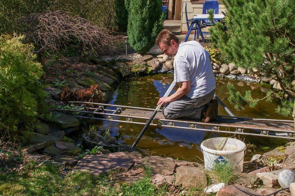 Man cleans garden pond with pond mud vacuum cleaner