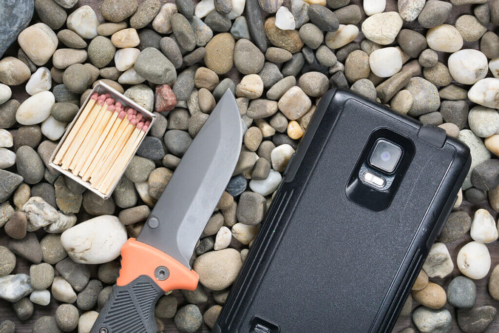 Knife, matches and smartphone on pebble floor