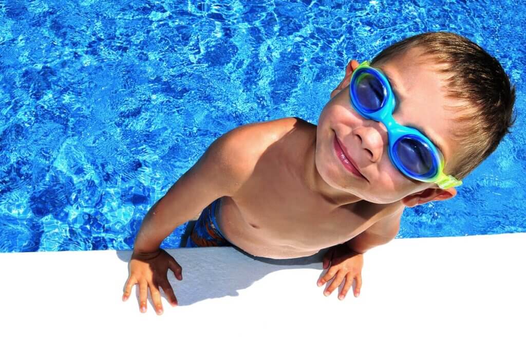 Child with swimming goggles gets out of pool